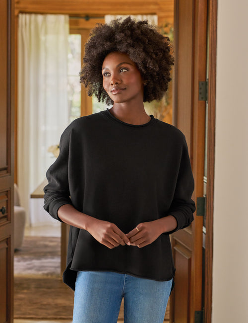 Woman wearing a black sweater and blue jeans standing in a doorway., front view