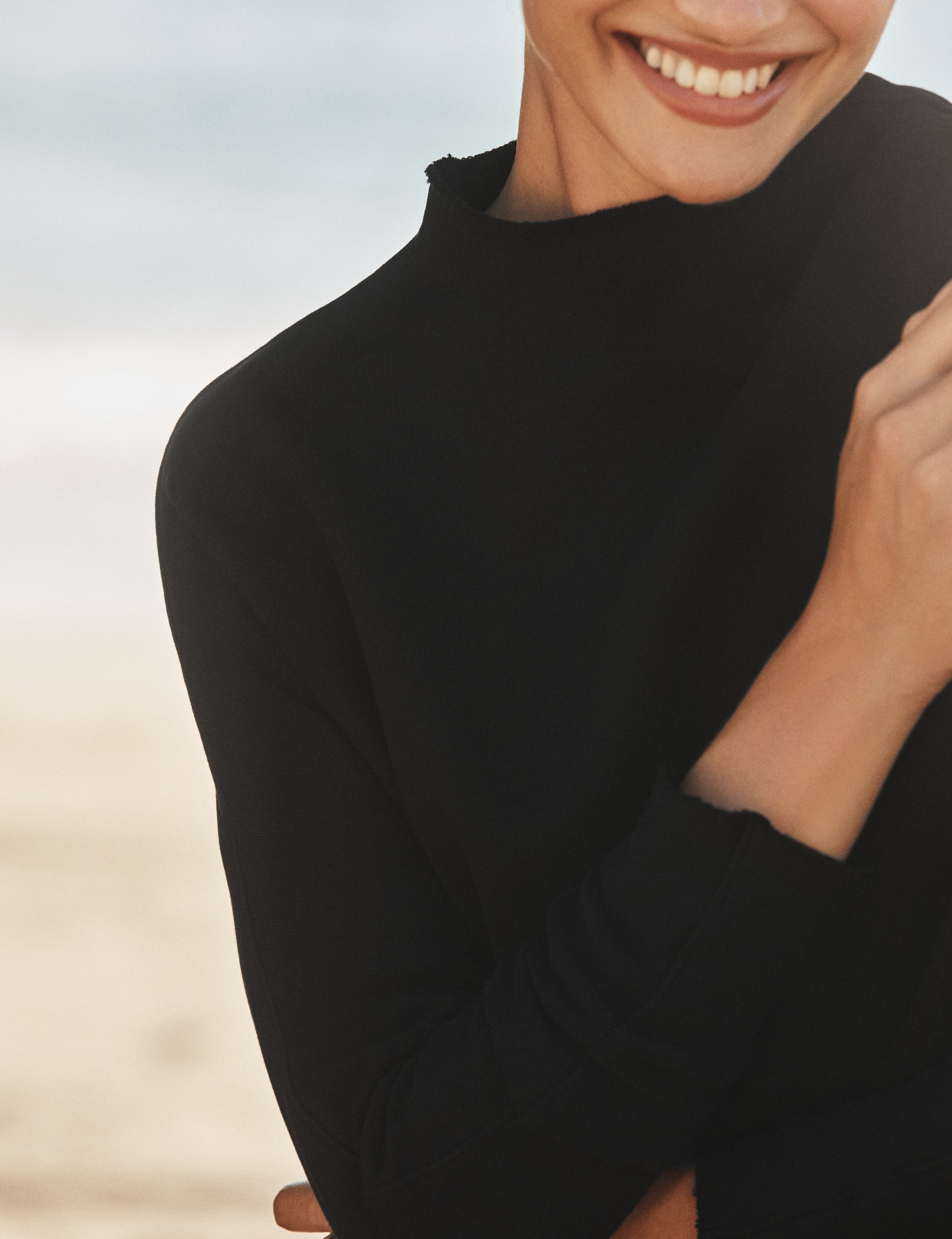 Person wearing a black long-sleeve shirt with a blurred beach background, view 3