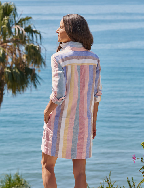 Woman wearing a colorful striped dress standing by a body of water with palm trees., alternate view