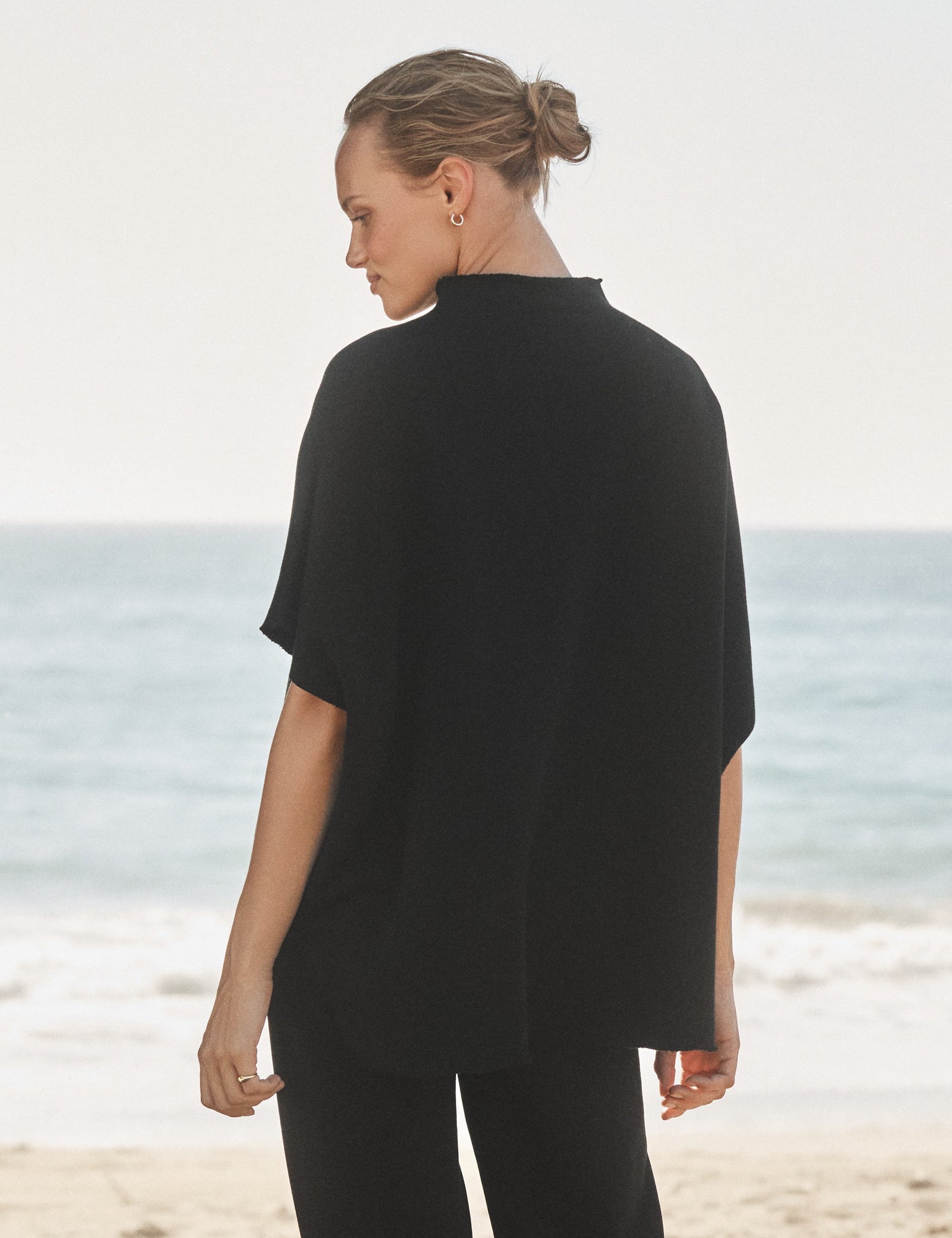 Woman in black outfit standing on a beach with ocean view, alternate view
