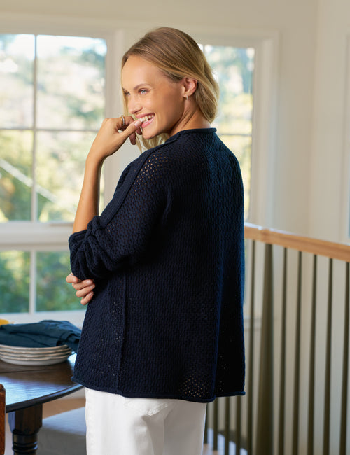 Woman wearing a navy blue eyelet sweater in a home setting, alternate view