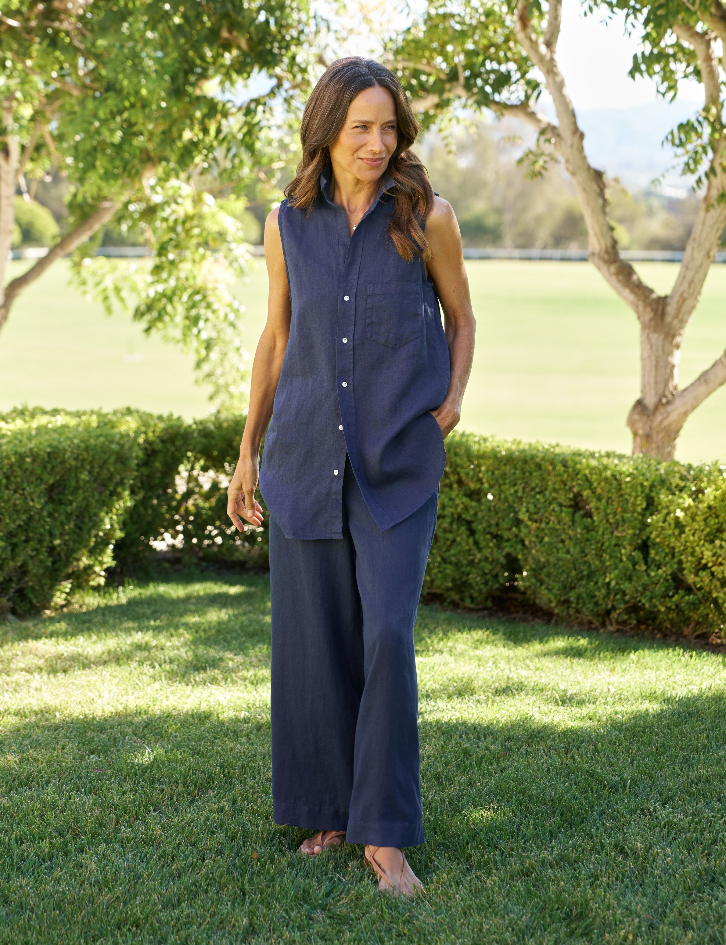 Woman in a blue outfit standing in a park-like setting with trees and grass.