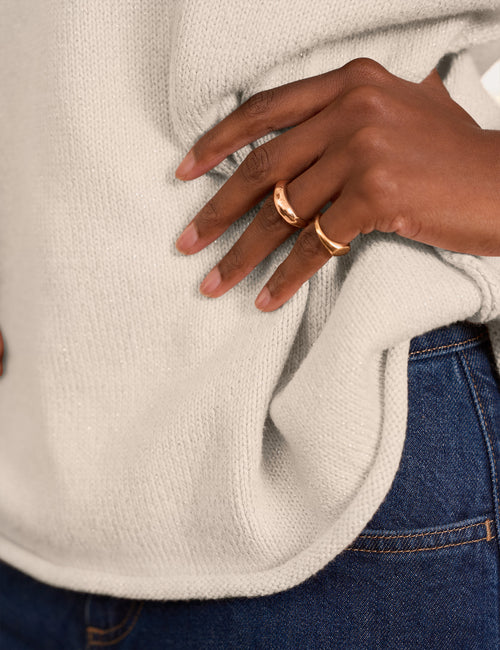 A close-up of a person wearing two slim rose gold rings on their fingers, styled with a cream knit sweater and blue jeans., view 3