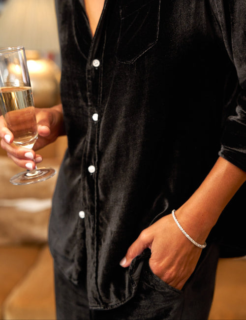 Person wearing a black velvet shirt holding a glass of wine indoors., view 3