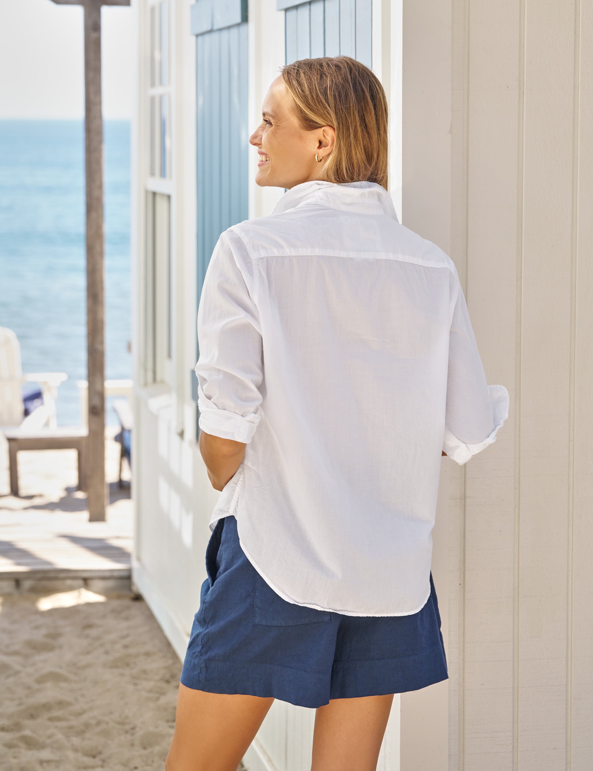 Woman wearing a white shirt and blue shorts standing on a beach., alternate view