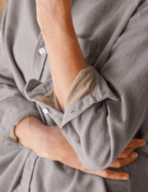 Close-up of a person wearing a soft gray long-sleeve shirt with rolled sleeves, showing a beige inner lining and white buttons., view 3