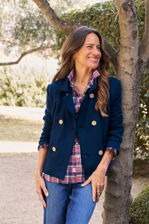 Woman standing outdoors next to a tree, wearing a navy jacket and blue jeans., front view