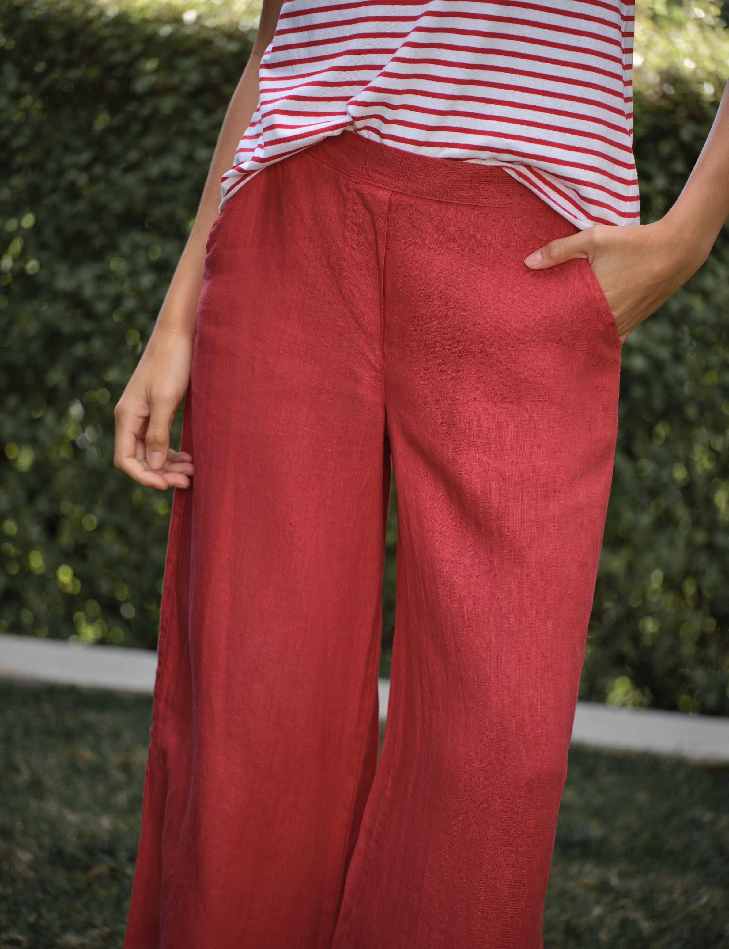 Person wearing red pants and a striped shirt against a green hedge background, view 3