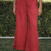 Person wearing red pants and a striped shirt standing in front of green foliage.