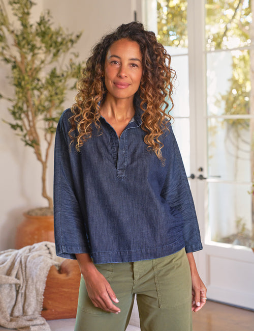 Woman wearing a blue denim shirt and green pants indoors, front view