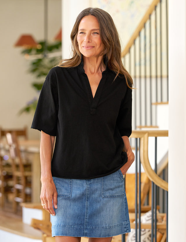 Woman wearing a black blouse and blue denim skirt in an indoor setting.