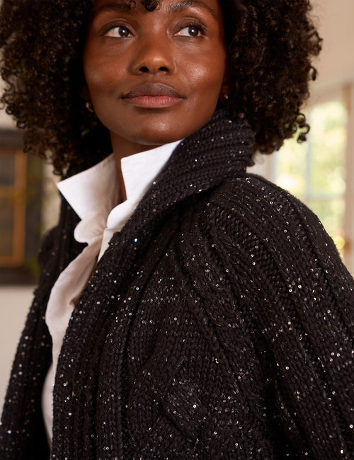 A close-up of a woman wearing a black cable-knit cardigan with silver sequins, layered over a white collared blouse., view 3