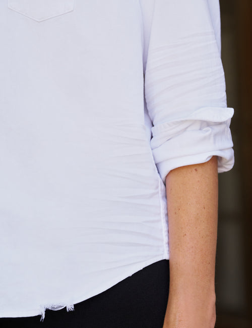 Close-up of a person wearing a white long-sleeve top with rolled sleeves and black bottoms, cropped from the chest down., view 3