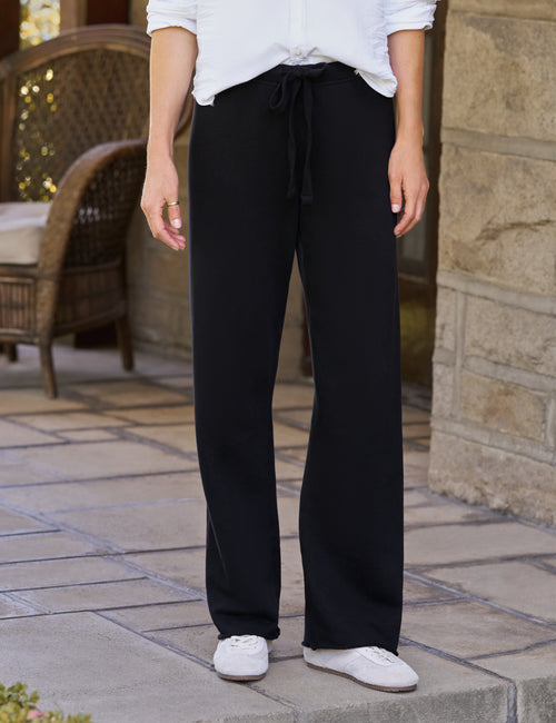 A person standing outdoors on a stone patio wearing black wide-leg drawstring pants, a white top, and white sneakers., front view