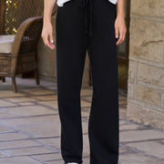 A person standing outdoors on a stone patio wearing black wide-leg drawstring pants, a white top, and white sneakers.