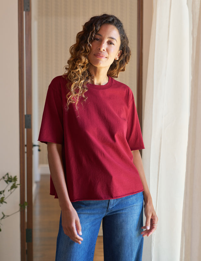Woman wearing a red t-shirt and blue jeans standing indoors.