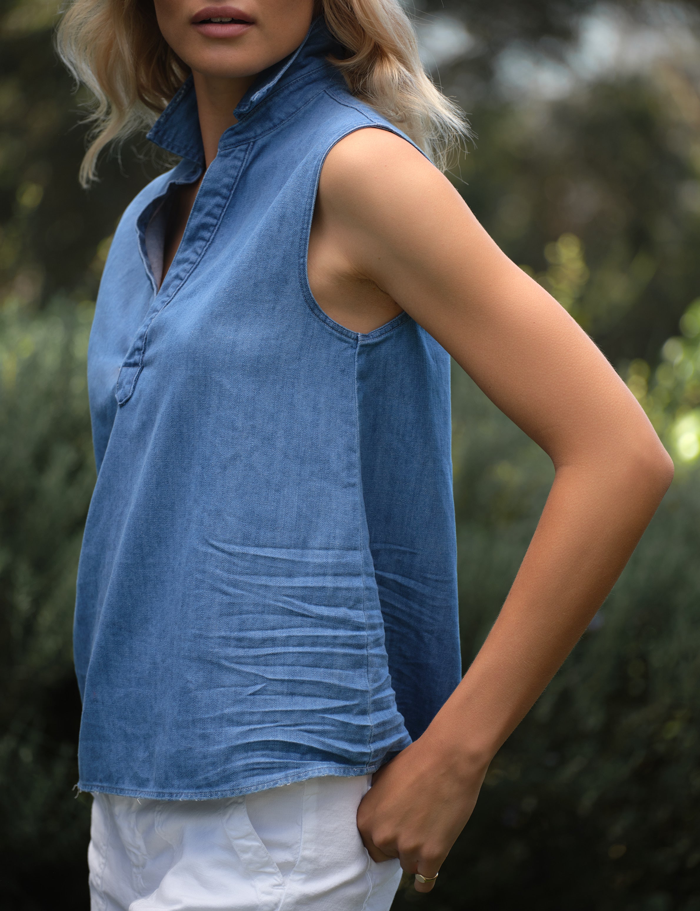 Woman wearing a blue sleeveless top with a blurred natural background, view 3