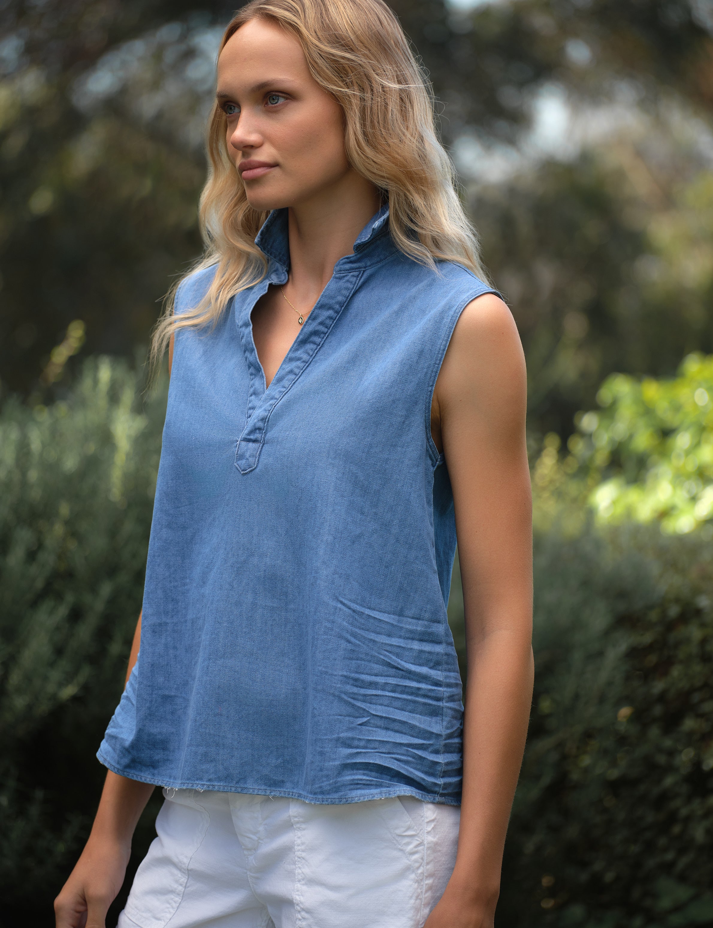 Woman wearing a blue sleeveless top with a blurred natural background, view 4