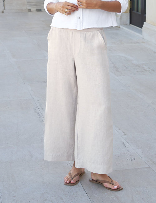 Woman in white shirt and beige pants standing in front of a classical building., front view