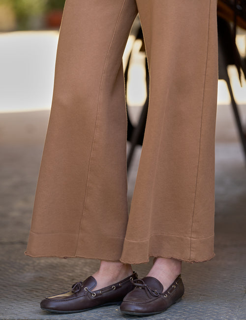 A close-up of a person wearing tan wide-leg pants and dark brown leather loafers, standing on a paved surface with a blurred outdoor background., view 3