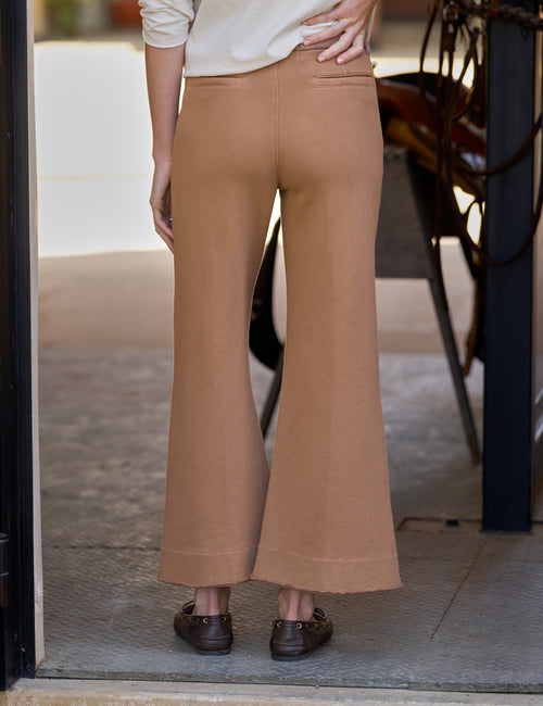 A person shown from the back wearing tan wide-leg cropped pants with a cream top and brown loafers, standing in a doorway., alternate view