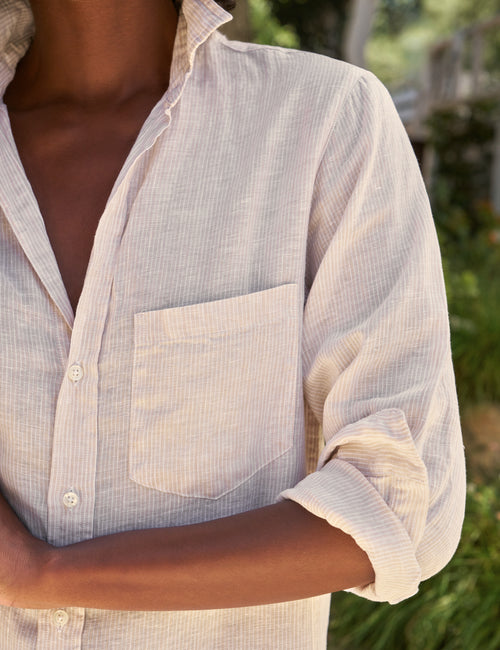Person wearing a light-colored striped dress with rolled-up sleeves in an outdoor setting., view 3