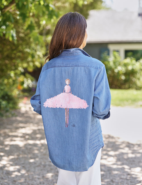 Person wearing a denim shirt with a pink ballerina design outdoors., front view