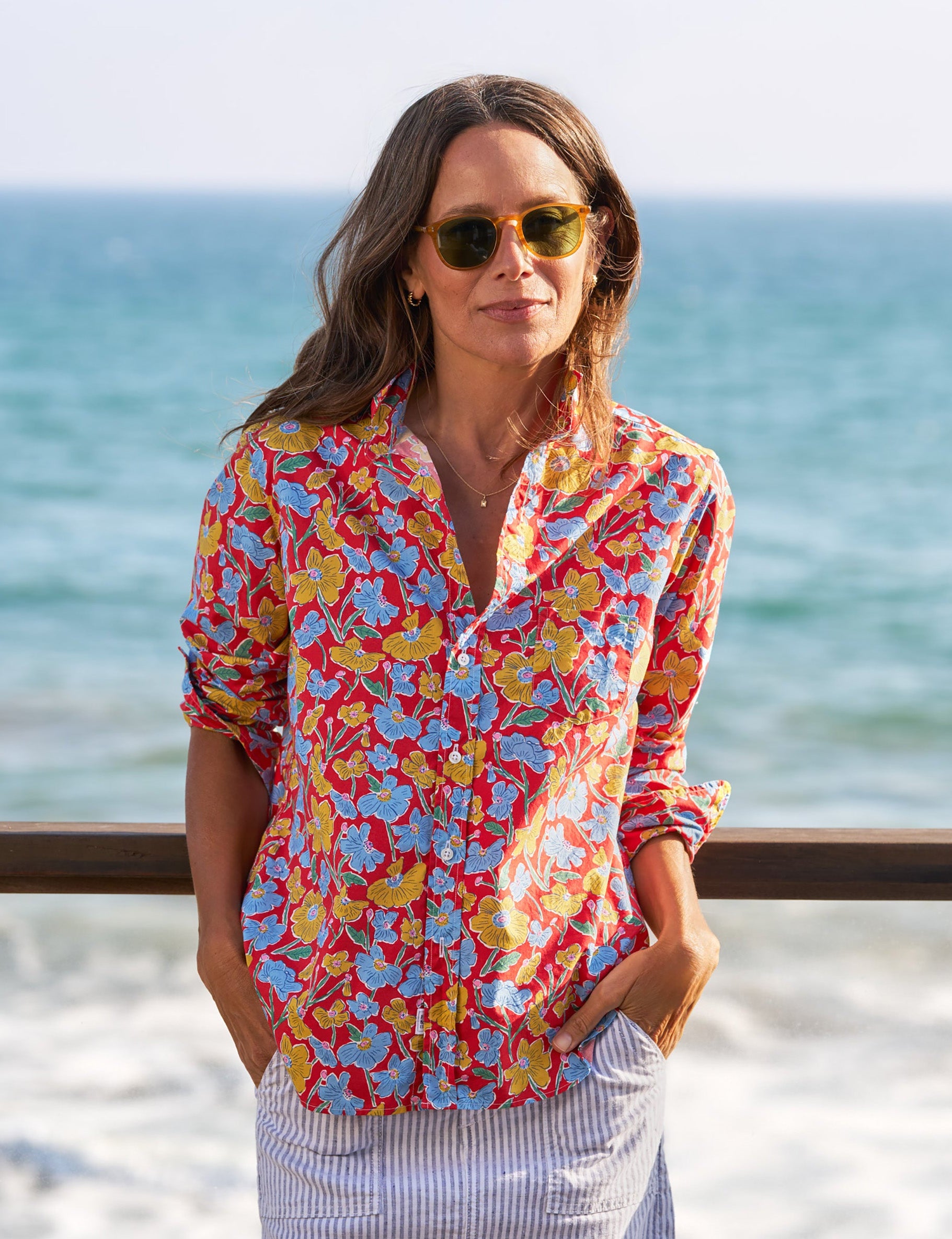 Woman wearing a colorful floral shirt and white skirt standing by the ocean., front view
