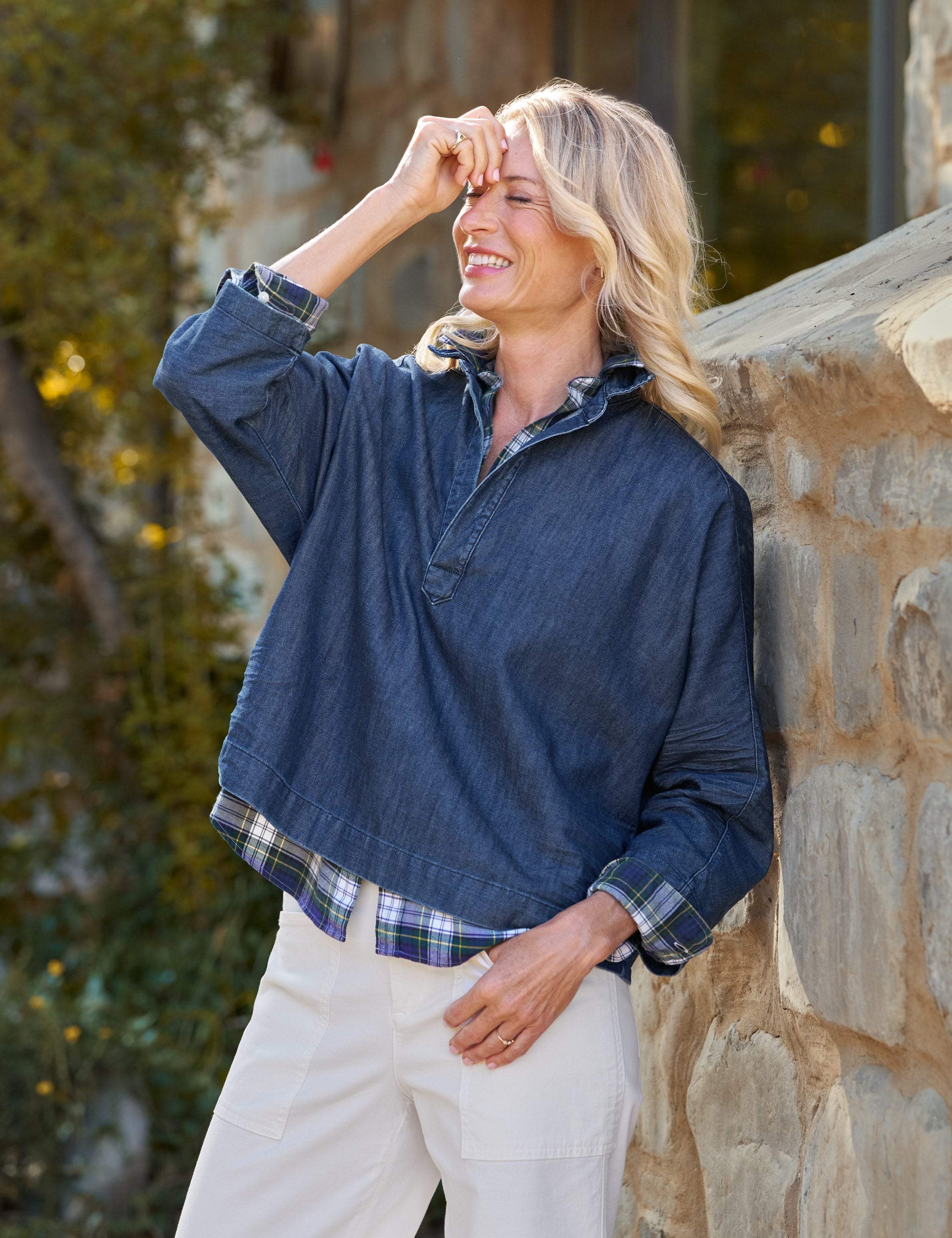 Woman wearing a blue shirt and white pants leaning against a stone wall.
