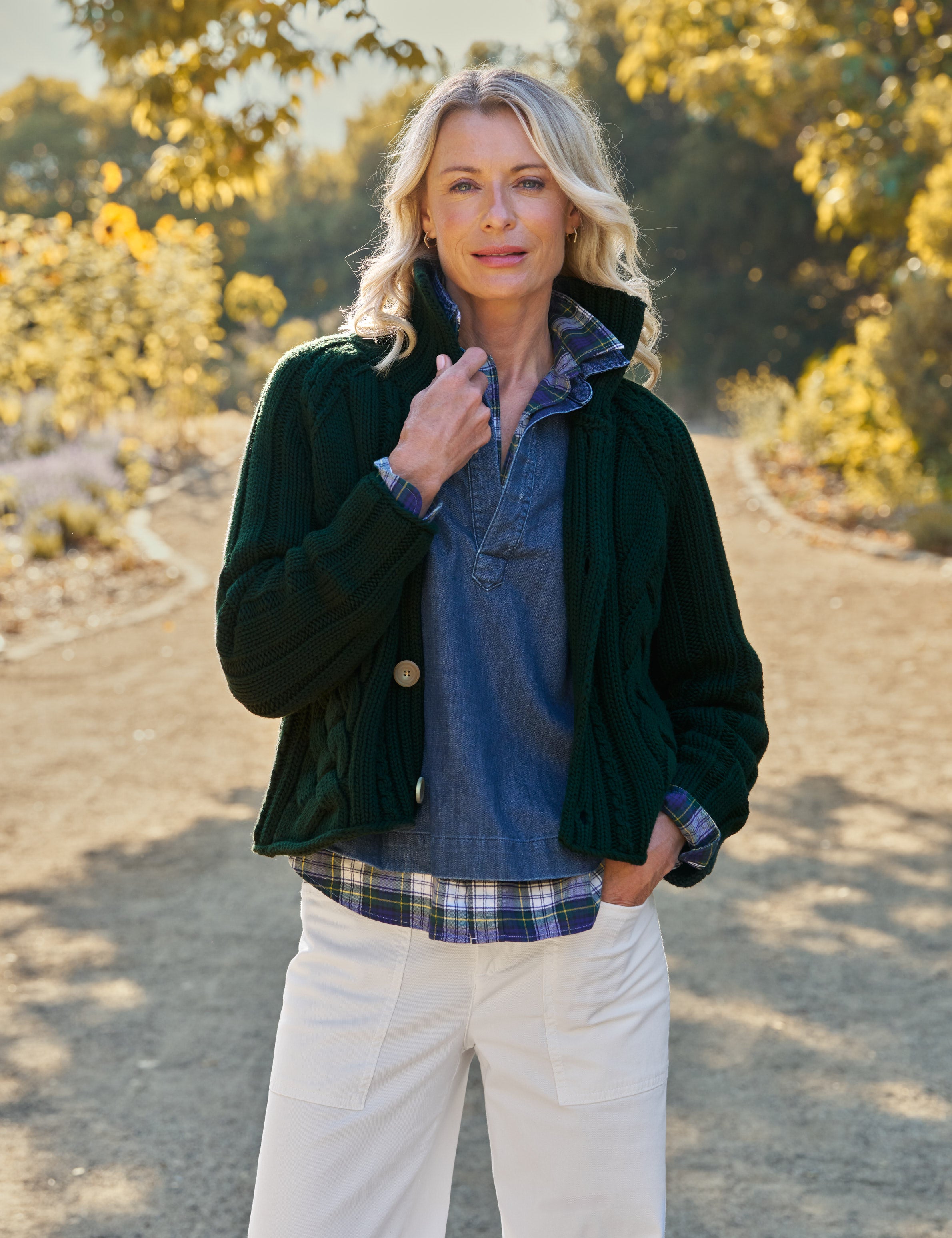 Woman standing outdoors in a natural setting wearing a dark green jacket and plaid shirt.