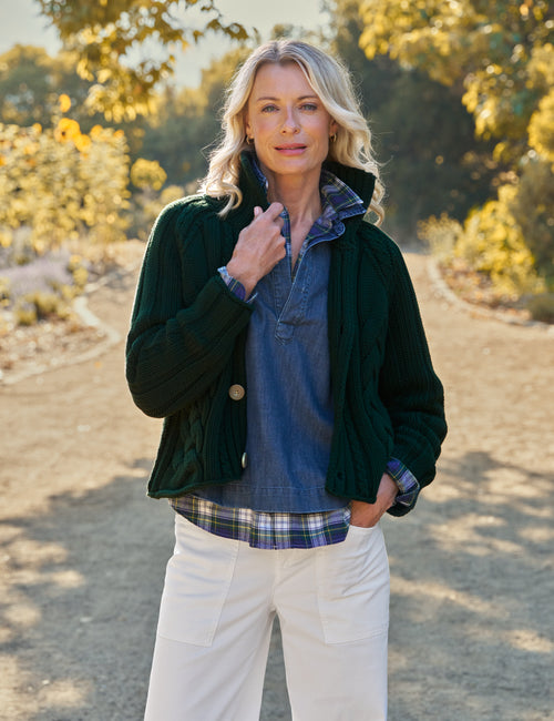 Woman standing outdoors in a natural setting wearing a dark green jacket and plaid shirt., front view