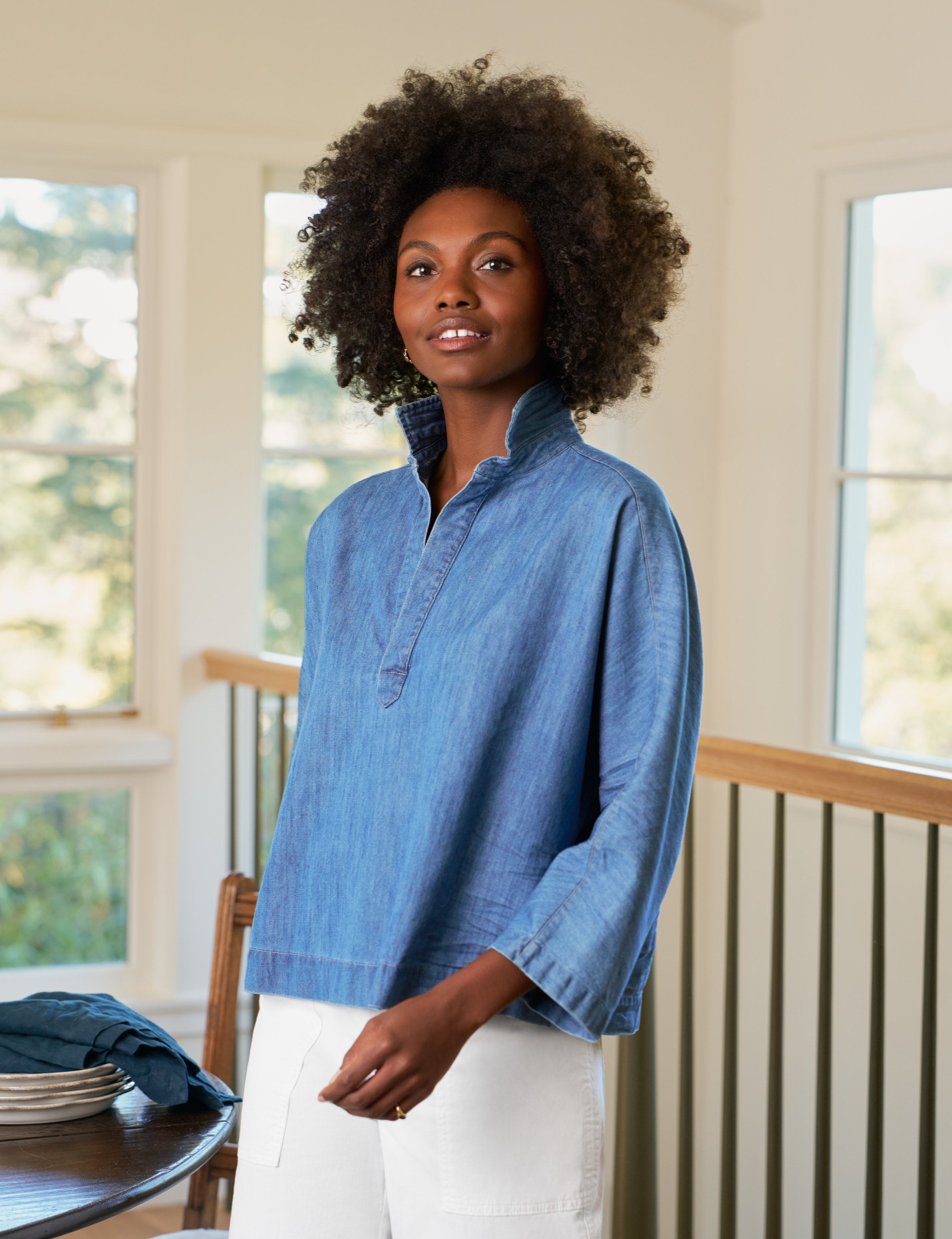 Woman wearing a blue shirt standing in a room with large windows.
