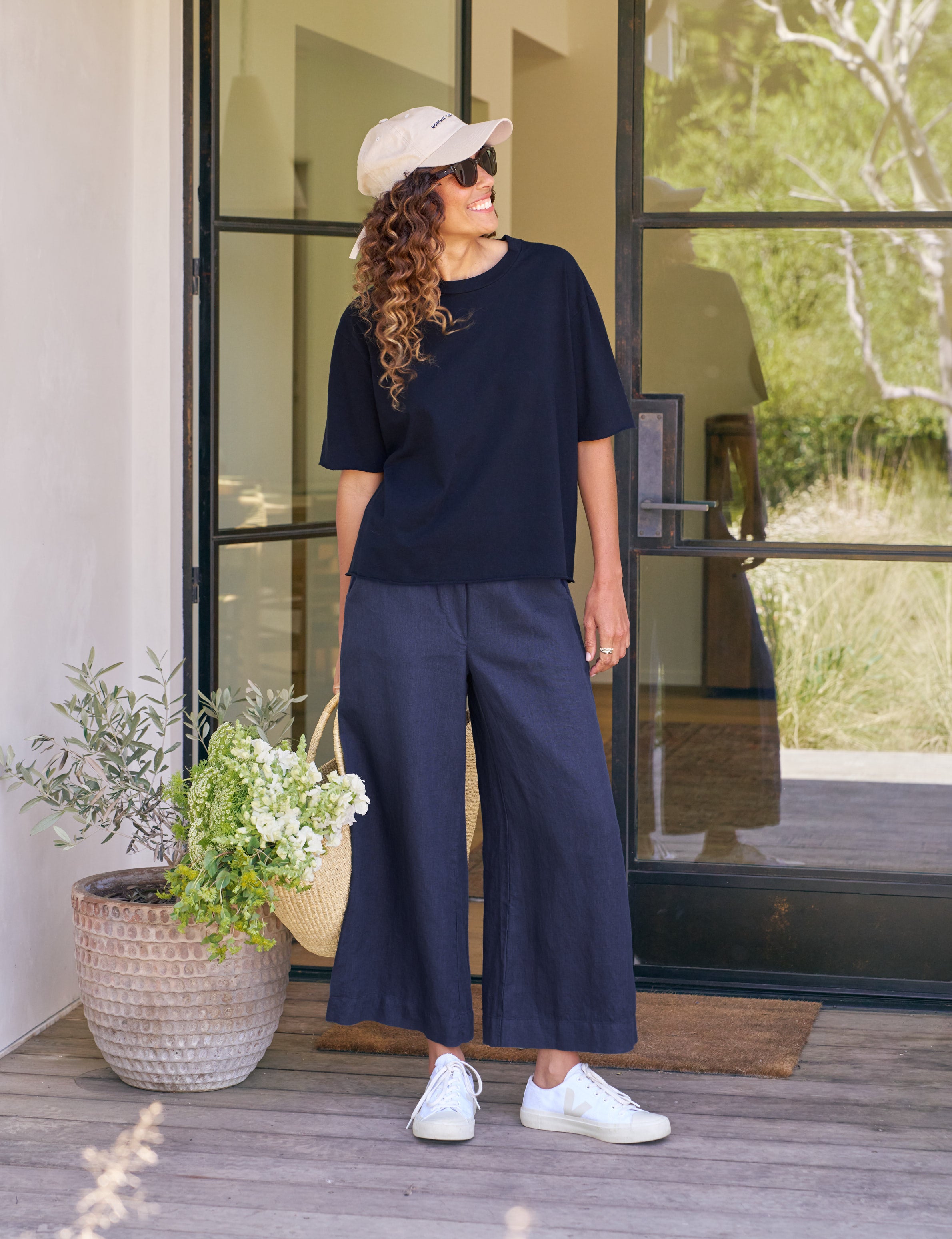 Woman in navy outfit standing on a wooden deck with plants and a glass door in the background, view 5