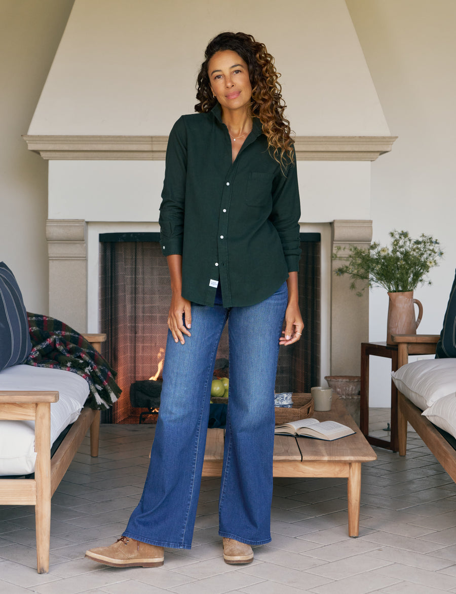 Woman wearing a dark green shirt and blue jeans standing in a living room with a fireplace.
