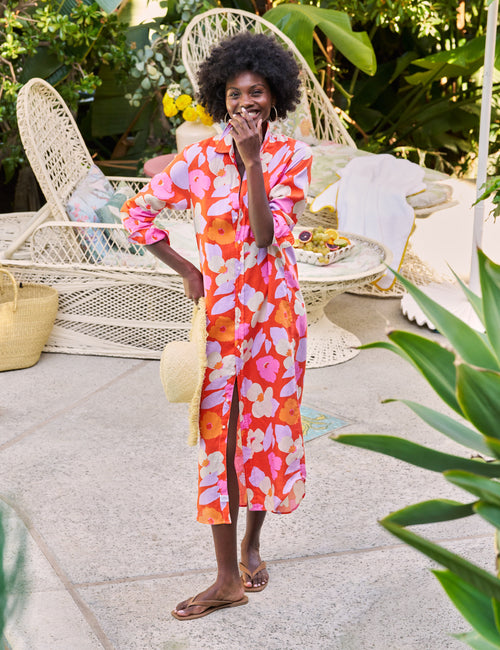 Woman in a colorful floral outfit standing outdoors with wicker chairs and plants in the background, view 5