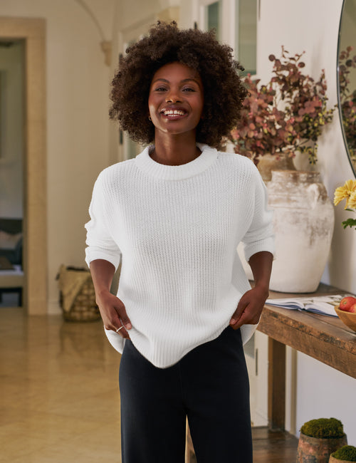 Woman wearing a white sweater in a home setting with decor elements., front view