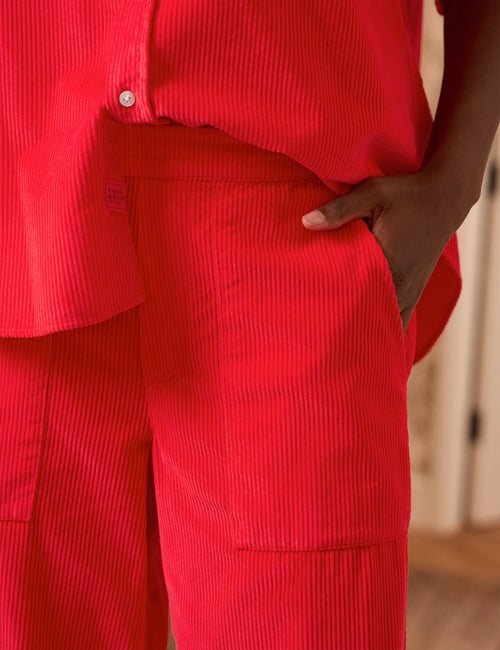 Close-up of a person wearing a bright red corduroy matching set, showing the waistband, front pocket, and hand in the pocket., view 3