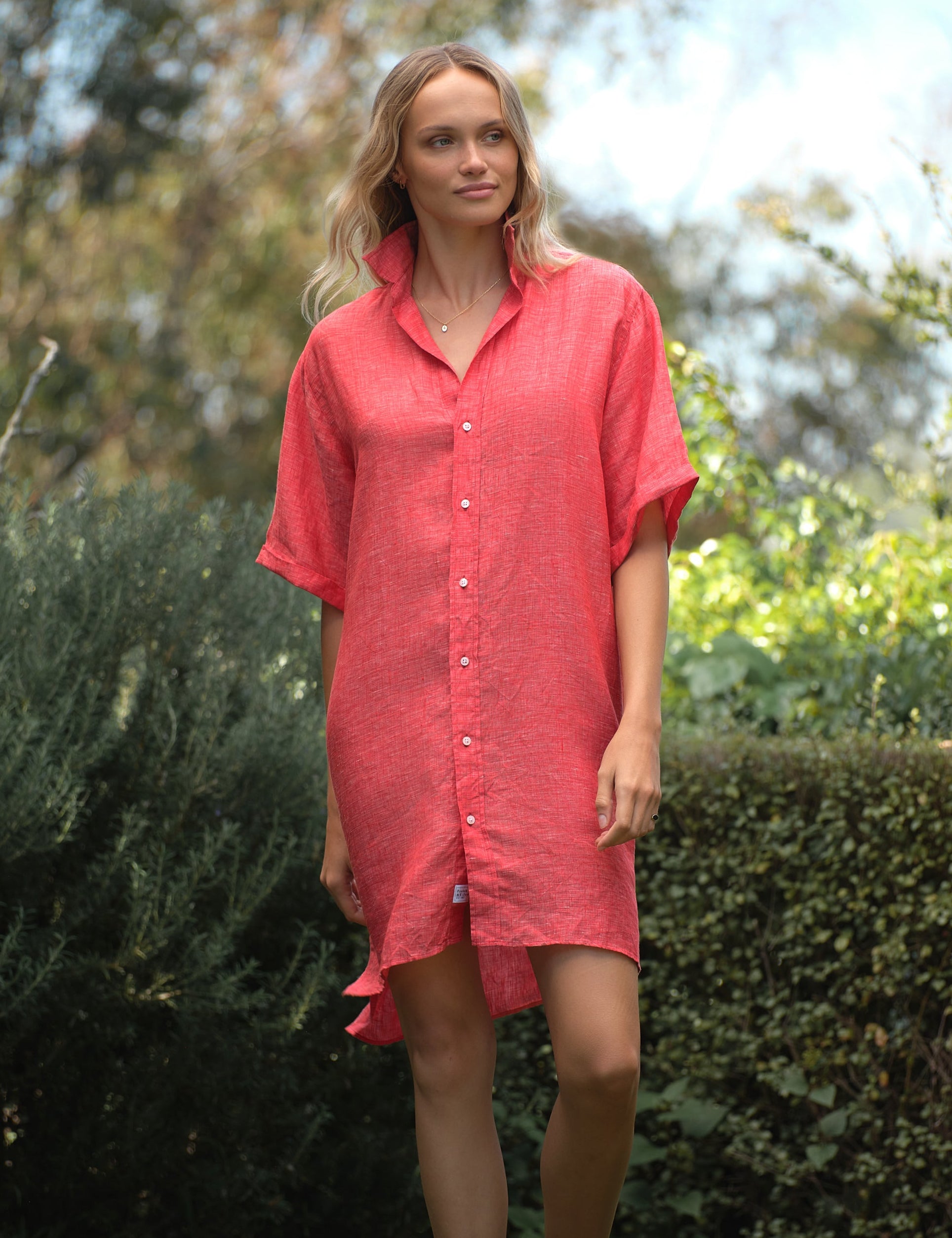 Woman wearing a red dress standing outdoors with greenery in the background, front view