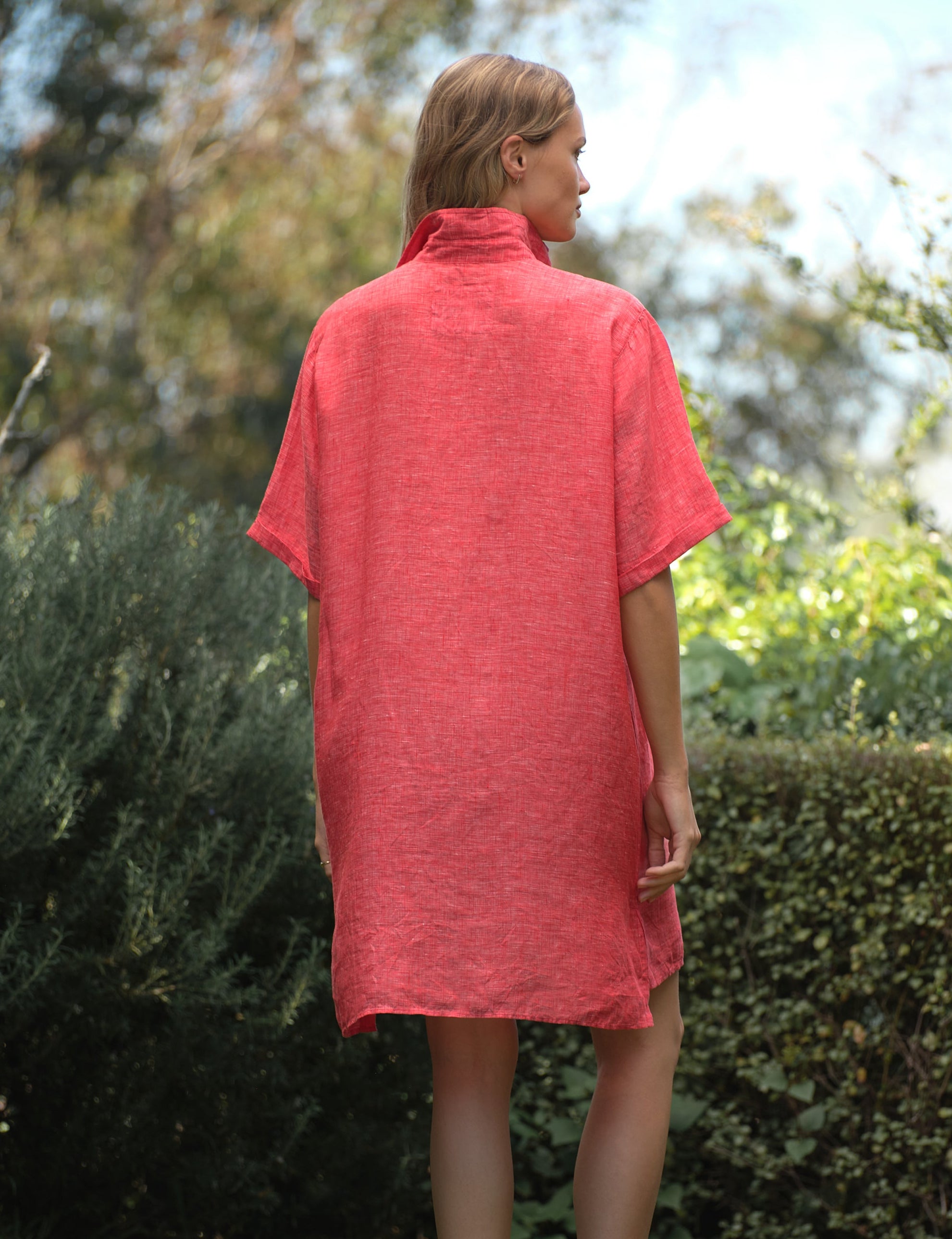 Woman wearing a red dress standing outdoors with greenery in the background, alternate view