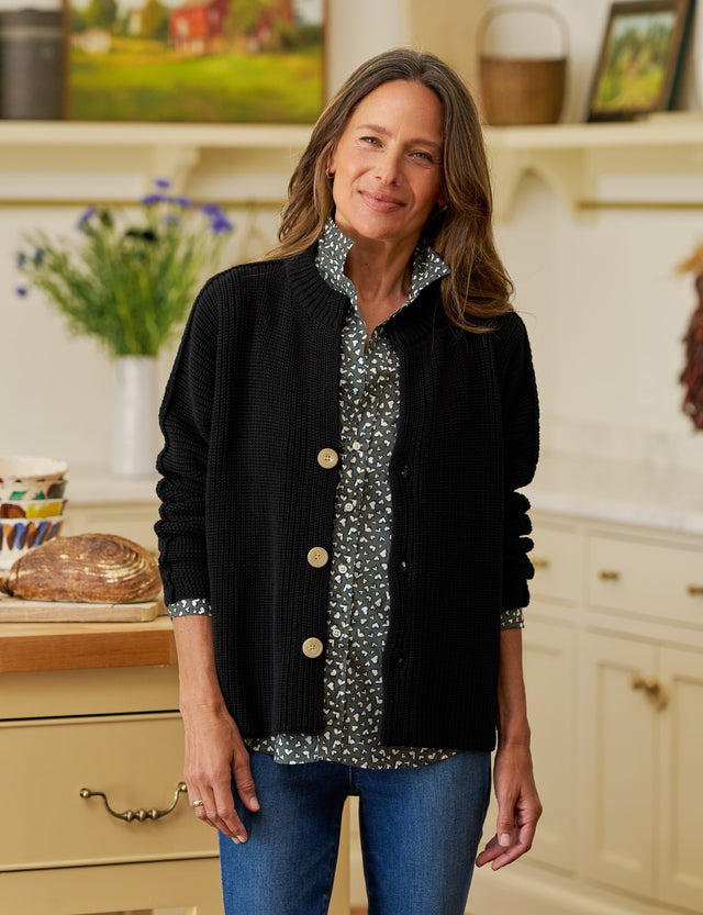 Woman wearing a black cardigan over a patterned shirt in a kitchen setting
