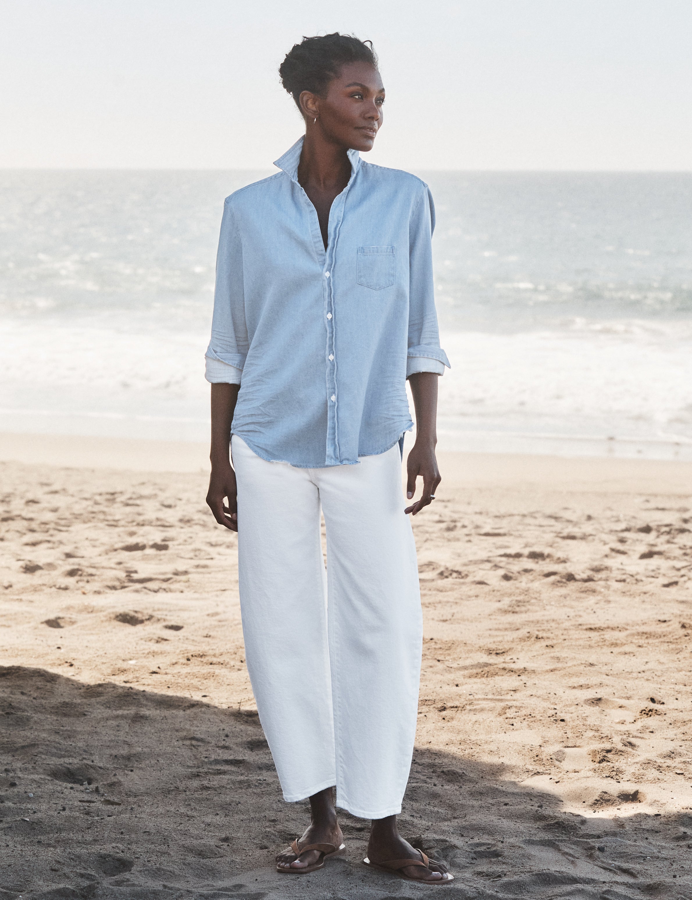 Woman wearing a light blue shirt and white pants standing on a beach., view 5