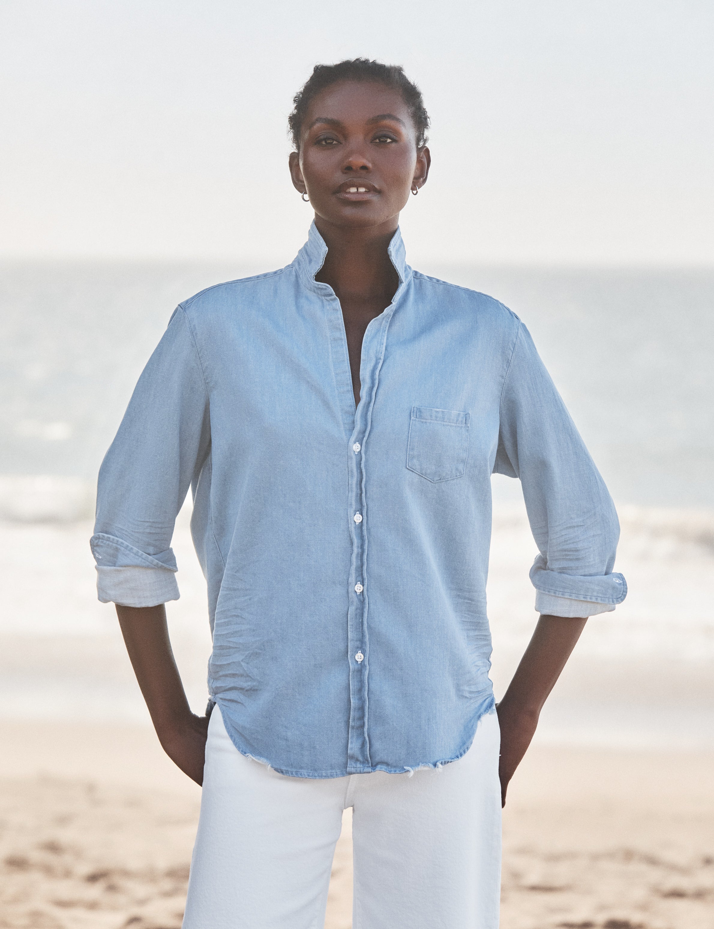 Woman wearing a light blue shirt and white pants standing on a beach., front view