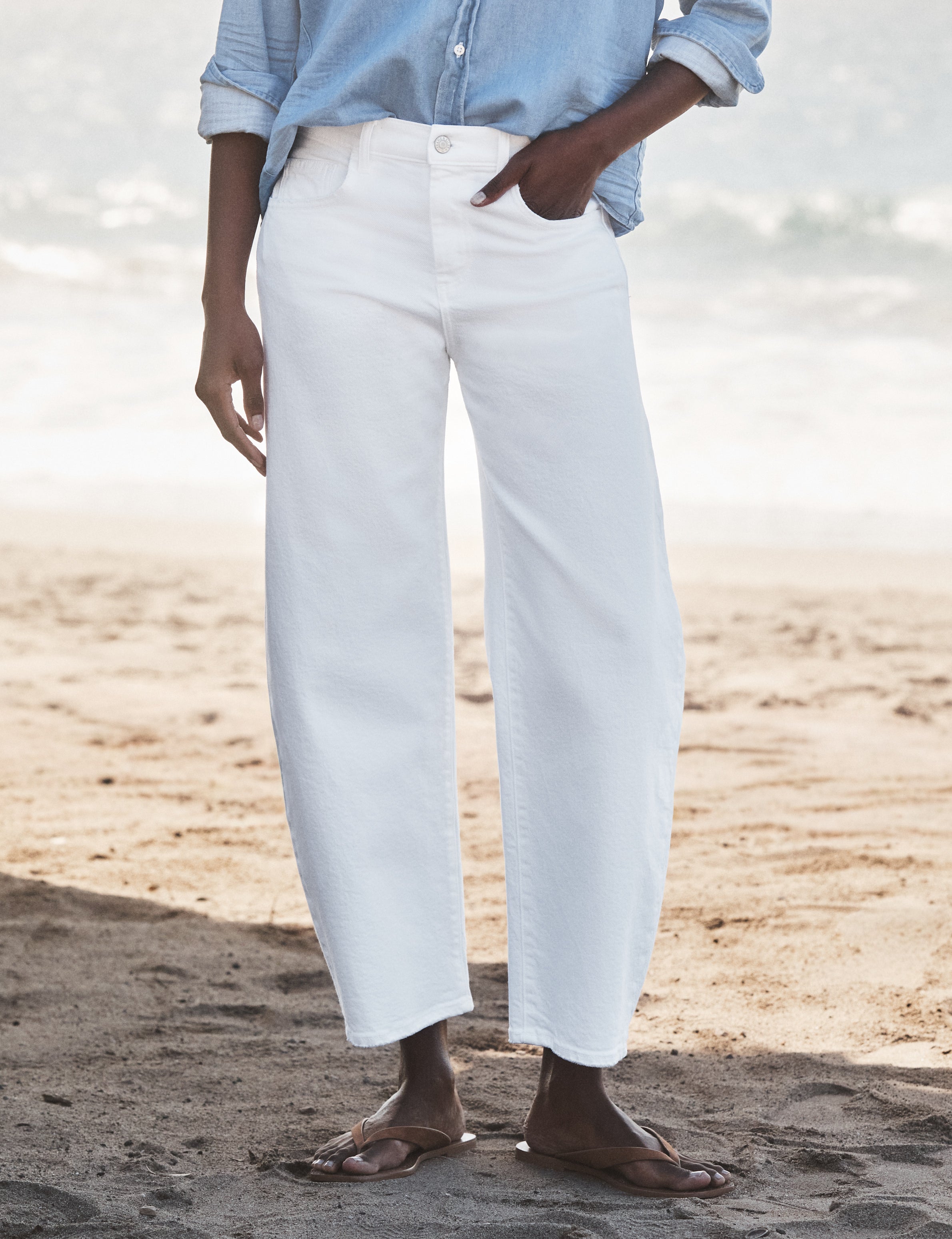 Person wearing light blue shirt and white pants standing on a sandy beach., front view