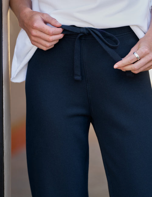 Close-up of a person wearing dark navy drawstring sweatpants and a white top, with hands adjusting the waistband and a ring visible on one finger., view 3