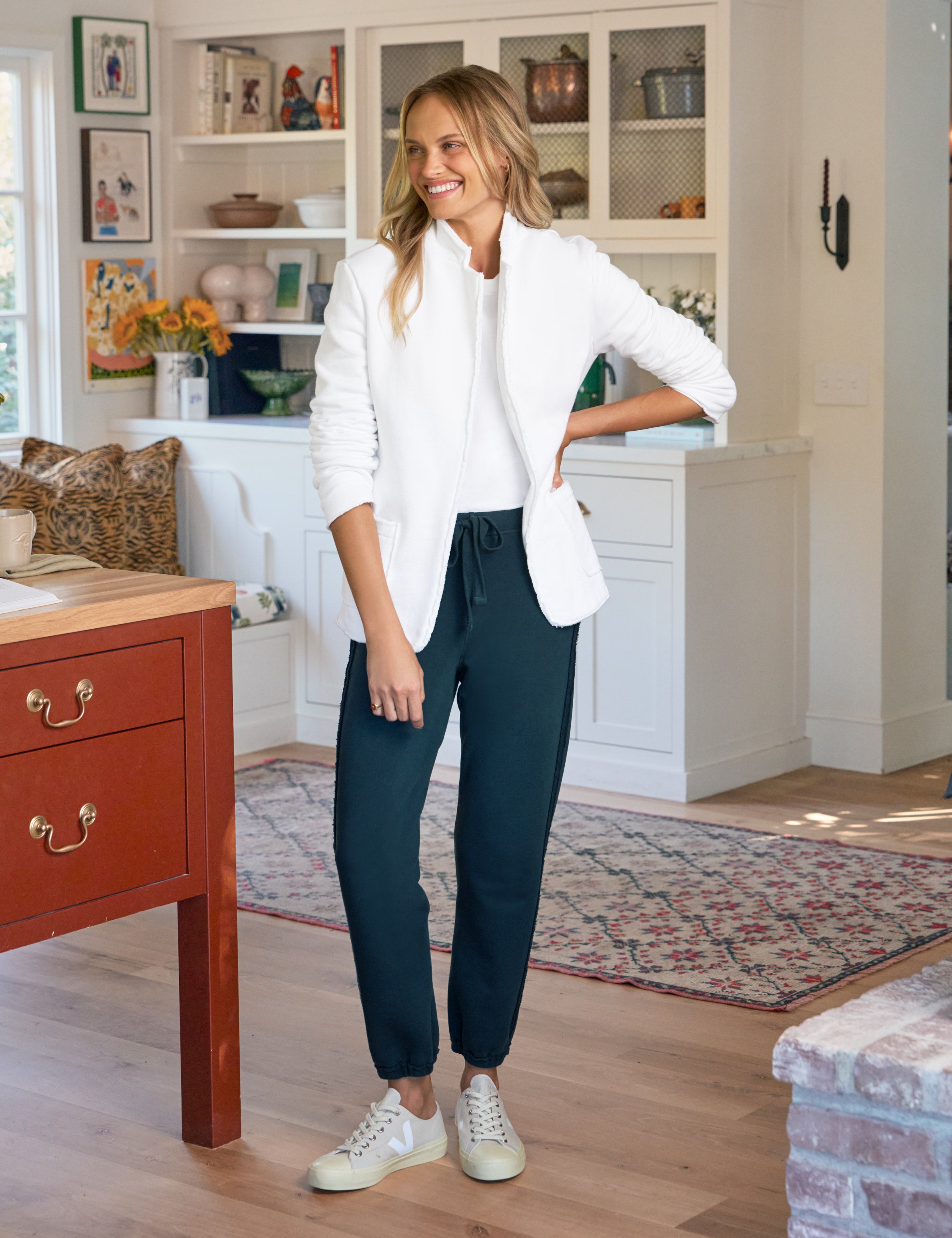 Woman in a white blazer and dark pants standing in a kitchen.