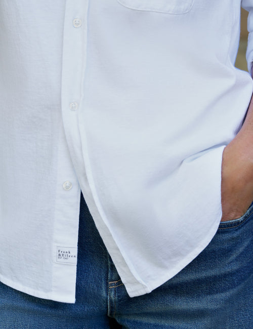 Close-up of a person wearing a white button-up shirt tucked into blue jeans, with the shirt pocket and front buttons visible., view 3