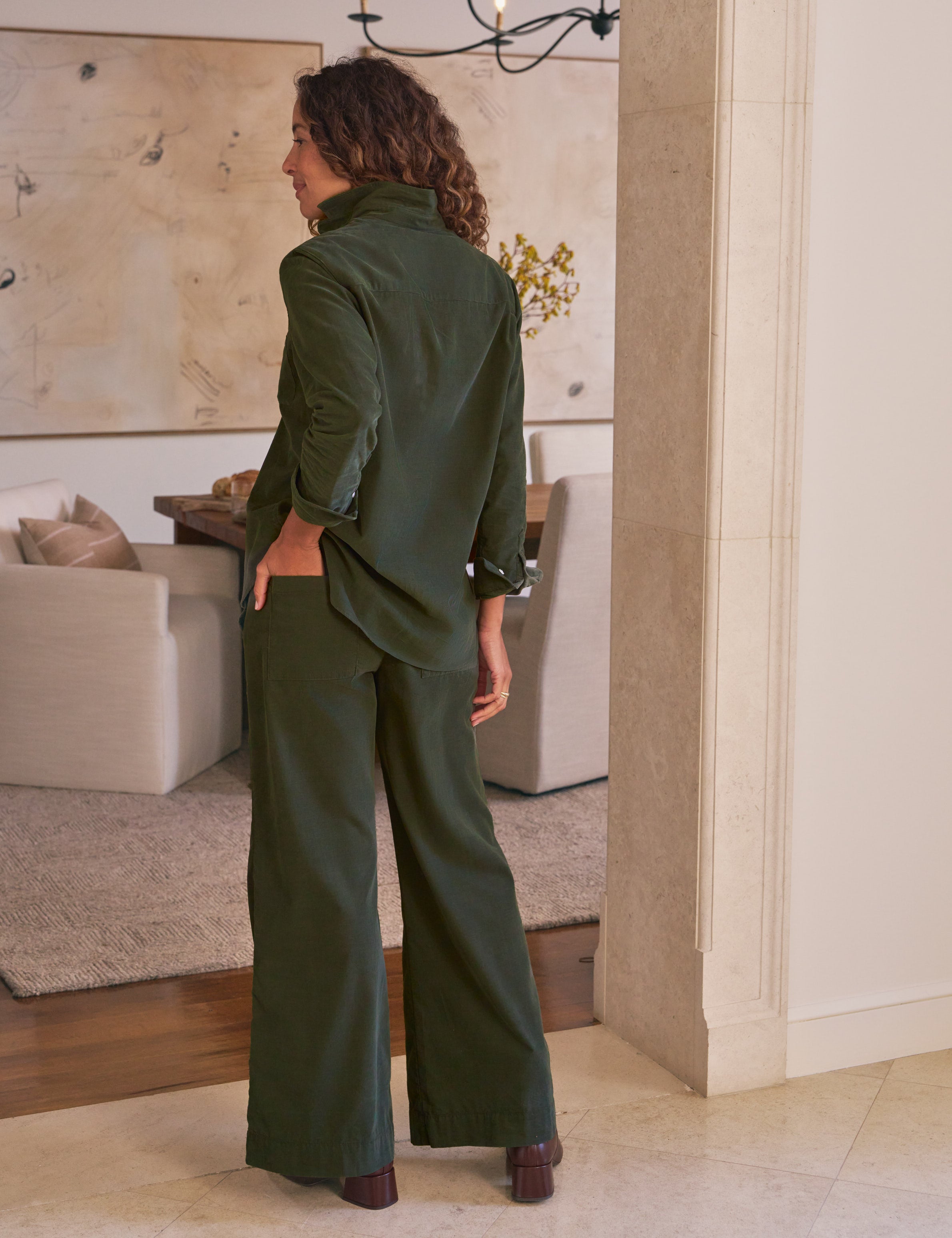 Woman in a green outfit standing in a room with a couch and decorative items.