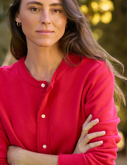 A woman wearing a bright red long-sleeve button-front top, photographed outdoors with a softly blurred natural background., view 3
