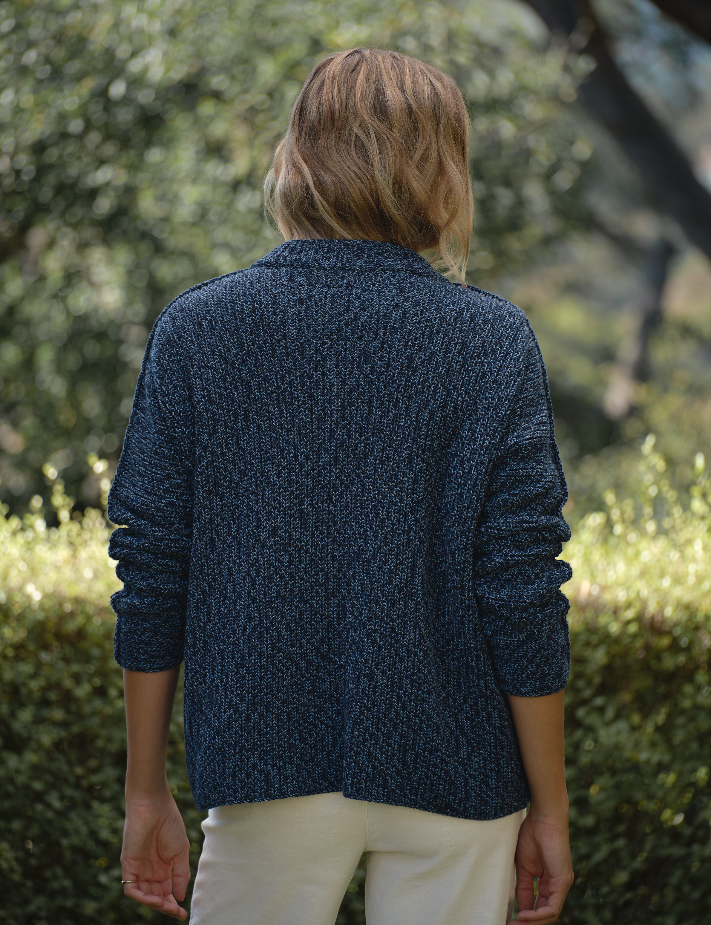Person wearing a blue knitted cardigan standing in a garden, alternate view