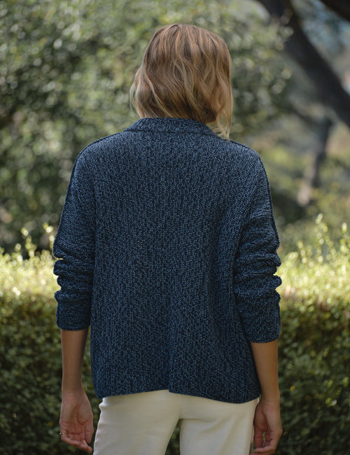 Person wearing a blue knitted cardigan standing in a garden, alternate view